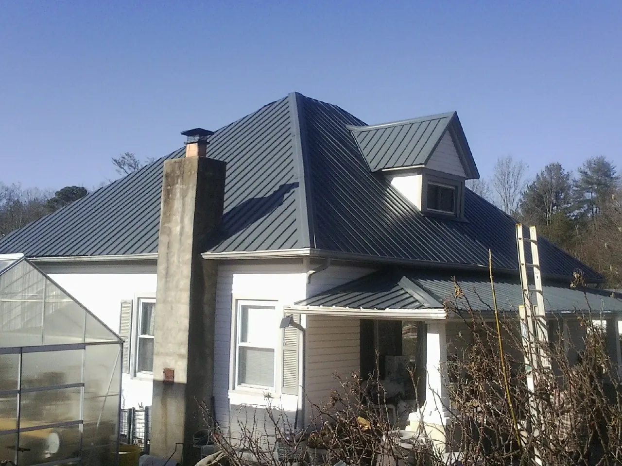 Dark blue standing seam metal roof on a white farmhouse with dormer — Slate & Tile Roof Repair by Roofing Brothers in Roulette