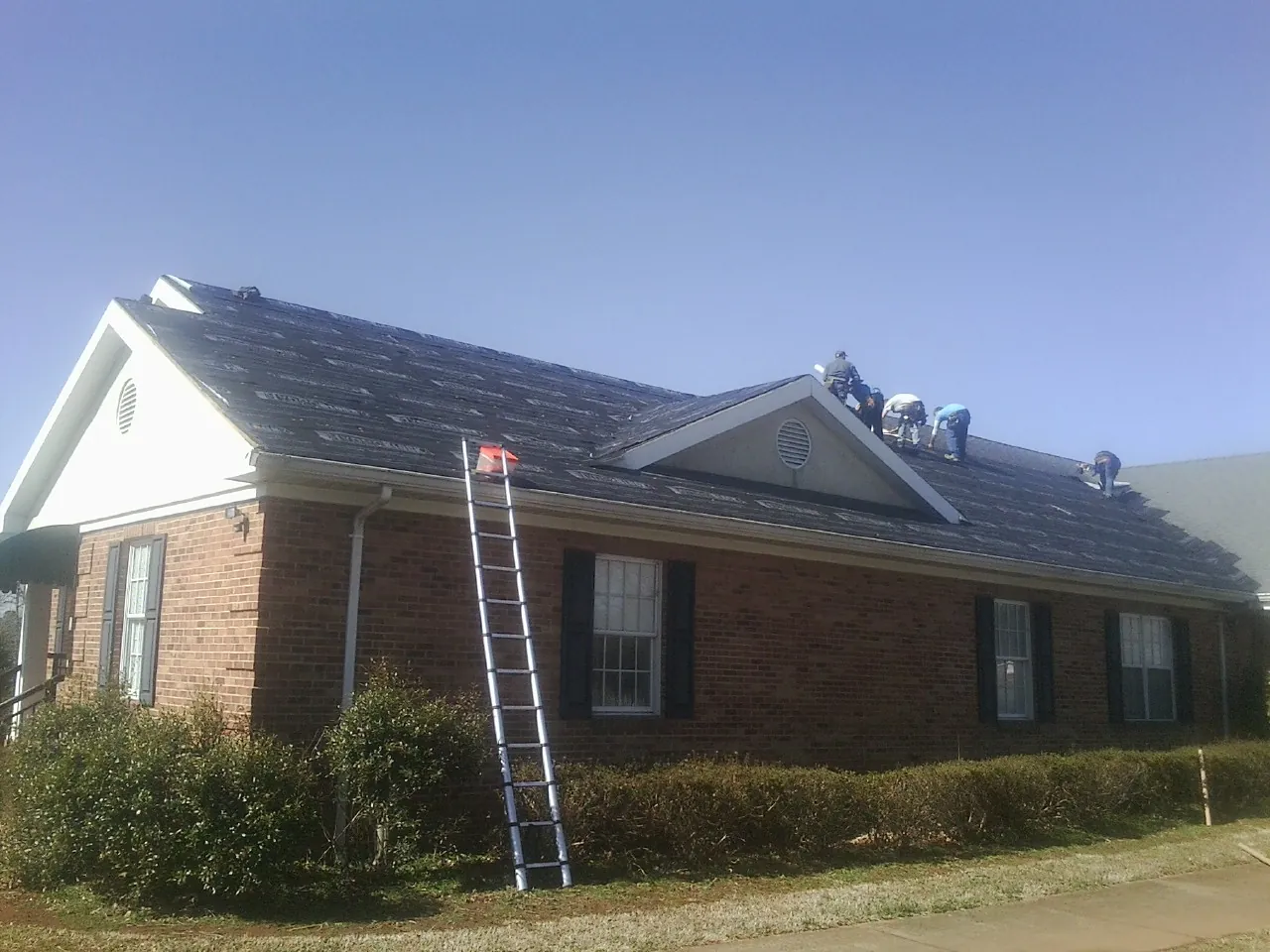 Crew tearing shingles off a brick ranch roof with a ladder set — Emergency Roof Repair work by our crew in Roulette