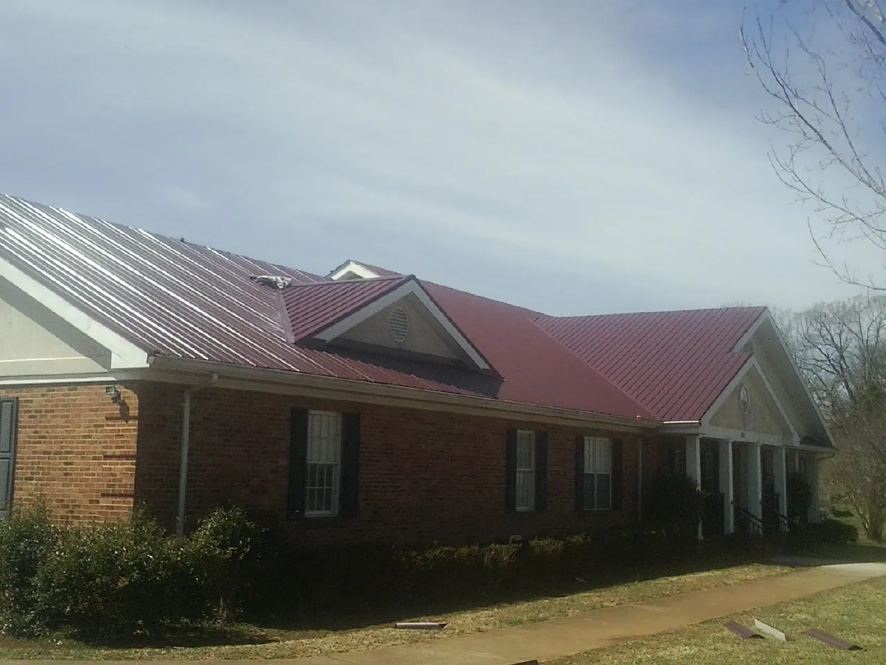 Red metal roof with gabled entries on a long brick building, from a Hail Damage Roof Repair job in Roulette