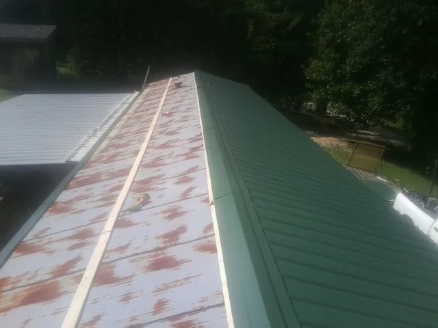 Old rusted panels beside newly installed green metal roofing — Wind Damage Roof Repair by Roofing Brothers in Roulette