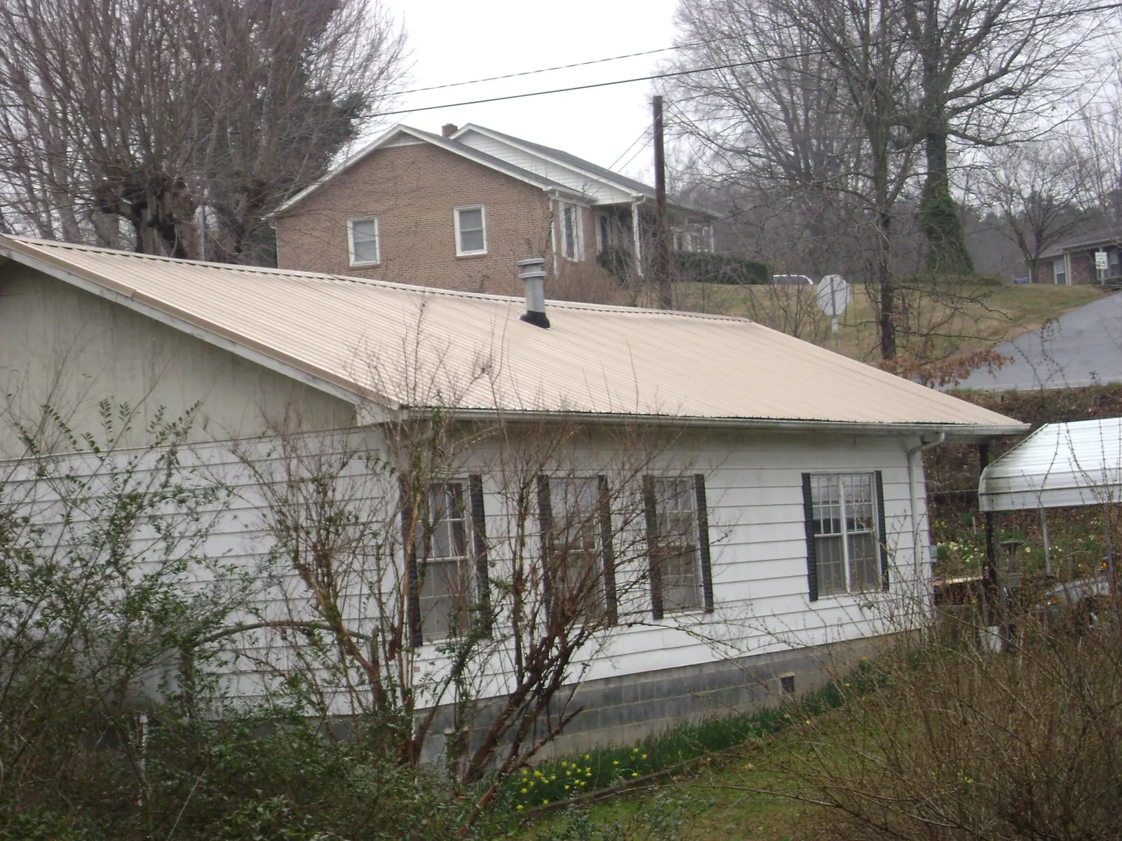 Tan metal roof on a white sided house set into a hillside — Commercial Roofing by Roofing Brothers in Roulette