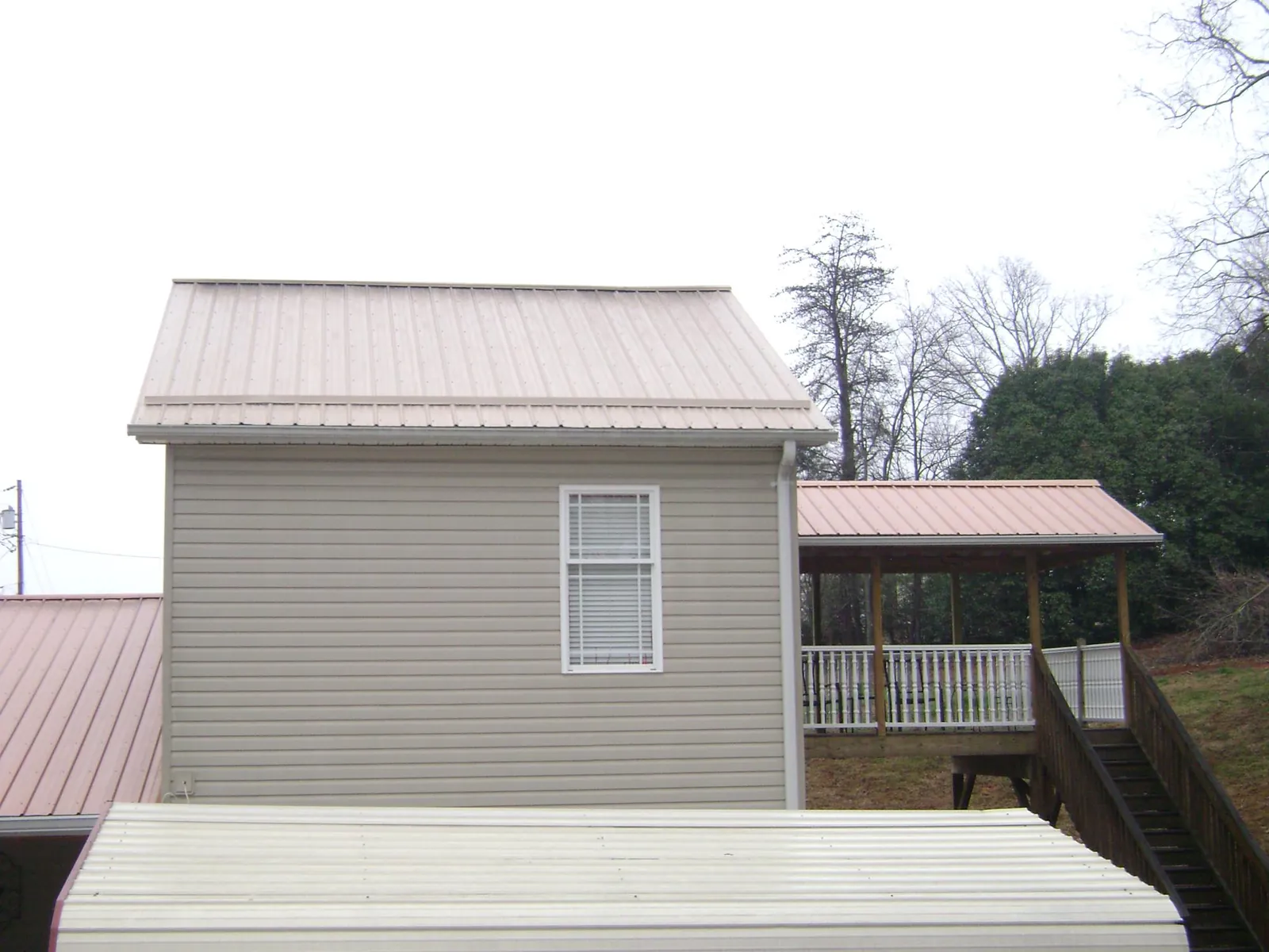 Tan metal roofs on a two story addition and attached porch, from a Roof Replacement job in Roulette